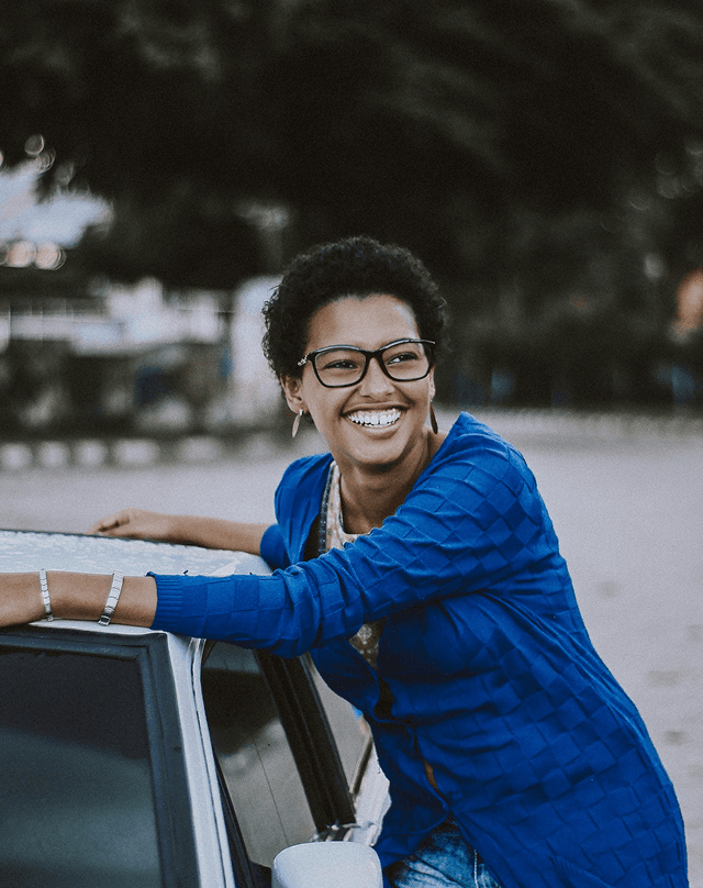 Smiling woman in glasses leaning on a car